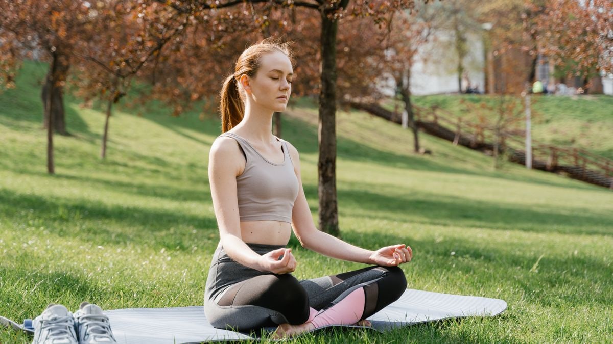 Woman meditating on a yoga mat in a park, promoting fitness and wellness.